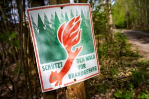Ein Schild mit der Aufschrift «Schütz den Wald vor Brandgefahr» hängt in einem Wald.