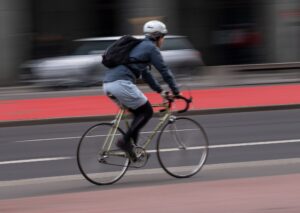 Ein Fahrradfahrer mit Helm fährt über einen Radweg an der Straße.