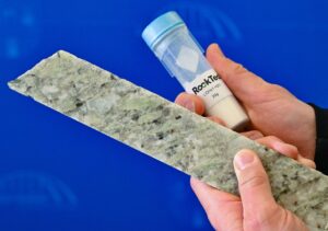 Ein Mitarbeiter von Rock Tech zeigt einen kleinen Behälter mit Lithiumhydroxid und das Lithium-Mineral Spodumen.