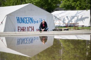 Wolfgang Metzeler-Kick sitzt am neuen Standort des Hungerstreik-Camps des Bündnisses «Hungern bis ihr ehrlich seid» im Regierungsviertel vor einem Banner.