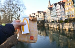 Eine McDonald's To-Go-Tüte und ein To-Go-Becher werden auf der Neckarbrücke in Tübingen vor der Kulisse der Altstadt gehalten (gestellte Szene).