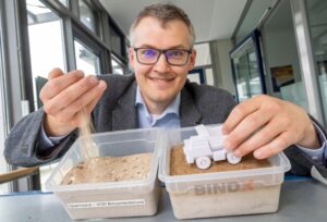 Luitpold Fried vom Start-Up-Unternehmen „Bind-X“ zeigt an einem Beispiel, wie mit einem speziellen Bindemittel aus ungefestigtem Sand, eine feste Verbindung entstehen kann, die zur Reduzierung von Staub auf unbefestigten Straßen führt.