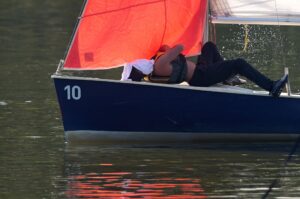 Puh, ist das warm: Ein Mann liegt im Schatten des Segels auf dem Deck eines Bootes auf dem Aasee in Münster und bedeckt sein Gesicht mit einem Handtuch.