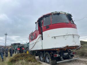 Mit mehreren Traktoren wurde der vor Sylt angespülte Aufbau eines ehemaligen Lotsenbootes hinter die Düne in Hörnum (Sylt) gezogen.
